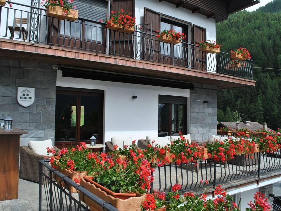 A hotel with outdoor seating, flower boxes on the balcony, and a stone facade.