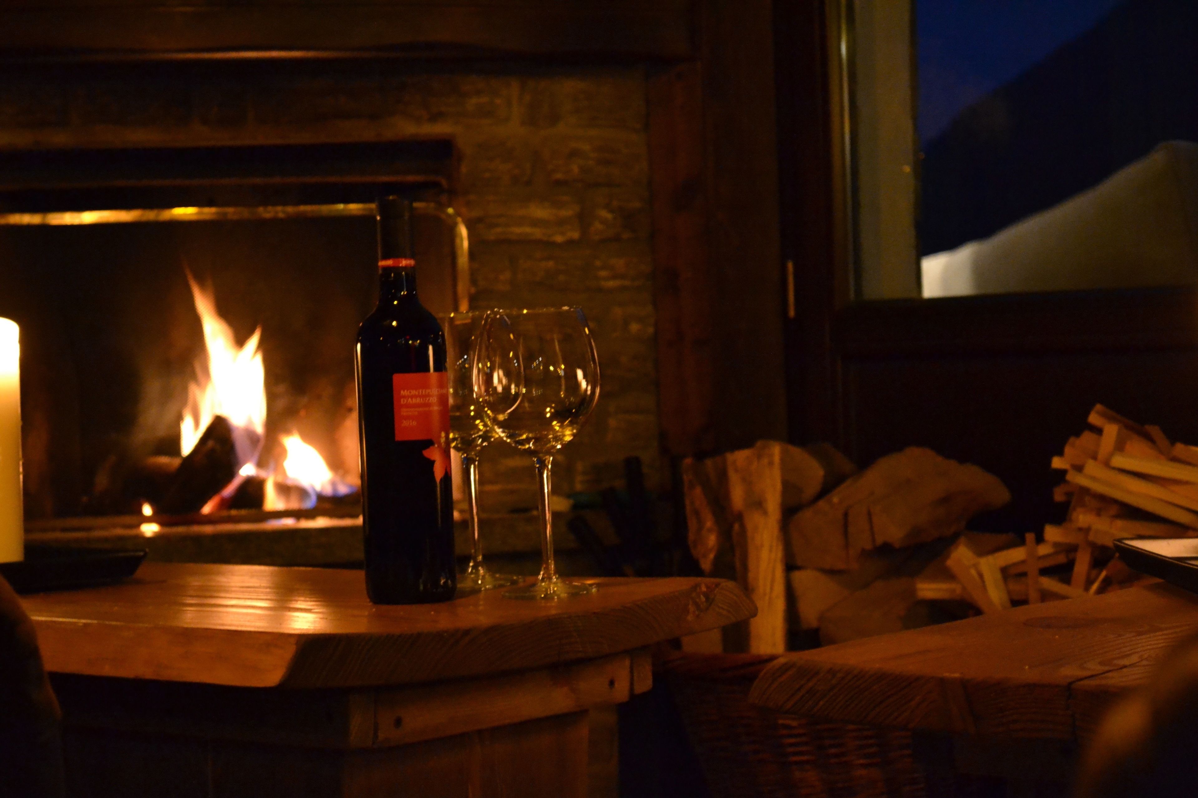 Una botella de vino y dos copas sobre una mesa de madera frente a una chimenea.
