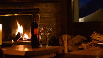 Una botella de vino y dos copas sobre una mesa de madera frente a una chimenea.