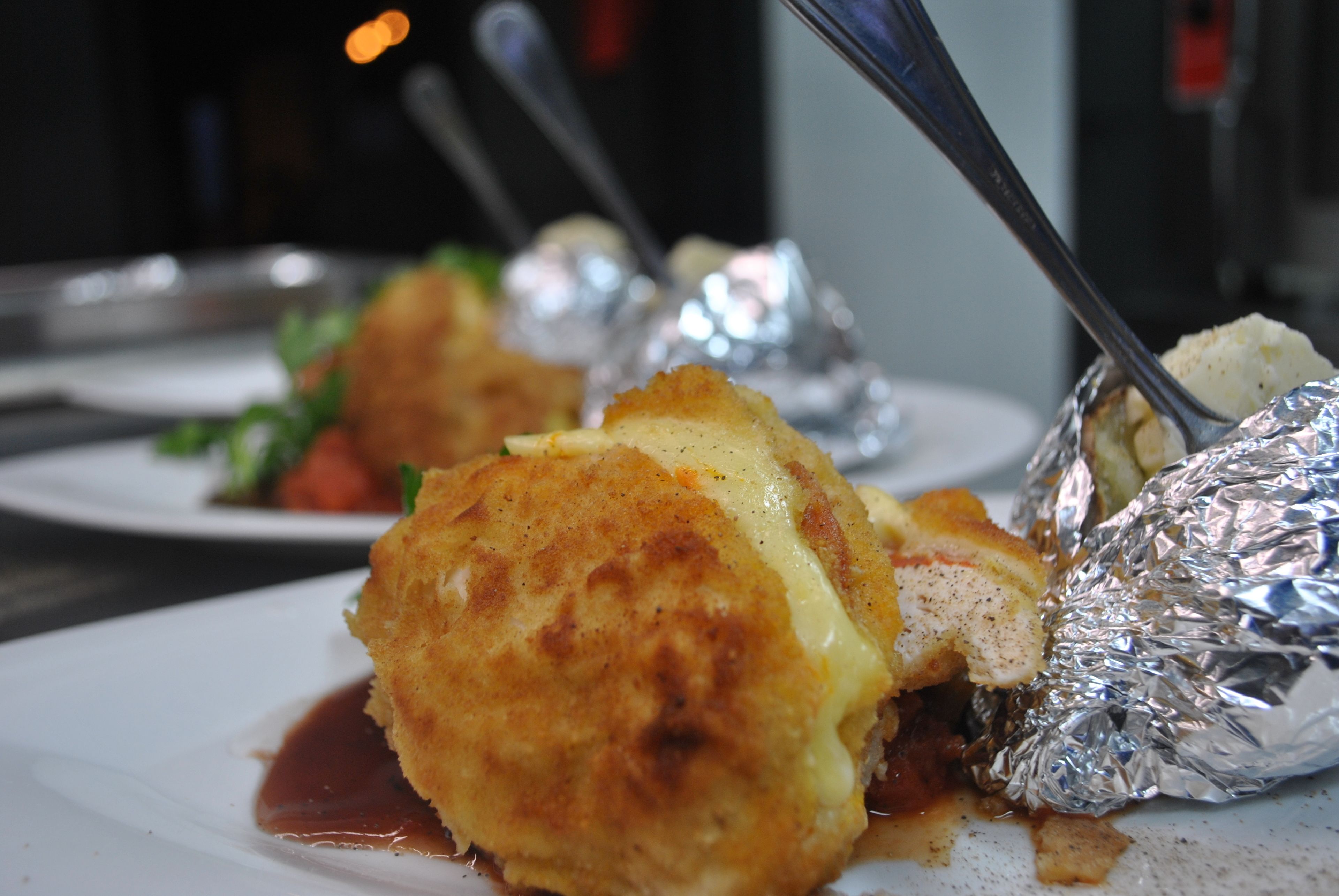 A close-up of a dish with a golden-brown crust, possibly a baked item, served on a white plate with a spoon.