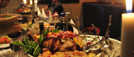 Una mesa de comedor con un centro de carne asada, rodeada de diferentes platos y vasos.