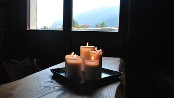 A candlelit table with four candles in a tray, positioned near a window with a view of mountains.