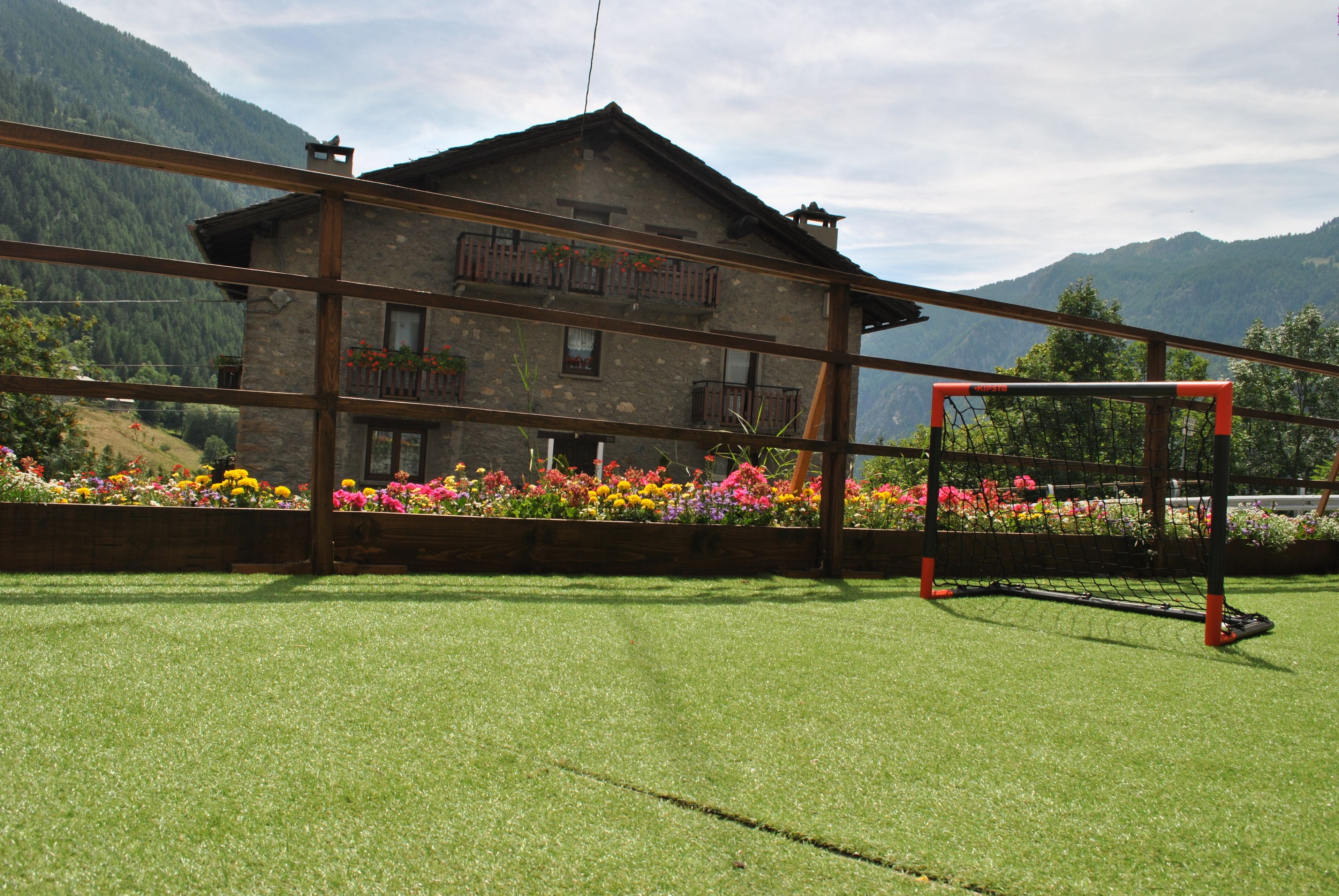 A building with a balcony, surrounded by colorful flowers and a mountain backdrop.