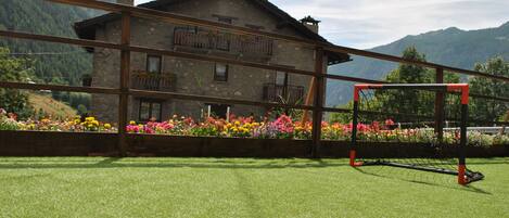 A building with a balcony, surrounded by colorful flowers and a mountain backdrop.