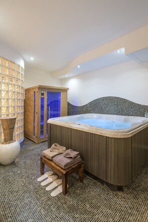A spa room with a hot tub, a wooden bench with towels, and a mosaic-tiled floor. - Rifugio degli Artisti Top (Rome)
