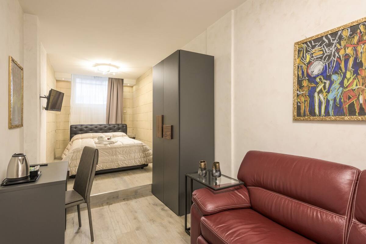 A hotel room with a bed, a desk, a leather sofa, and a painting on the wall.