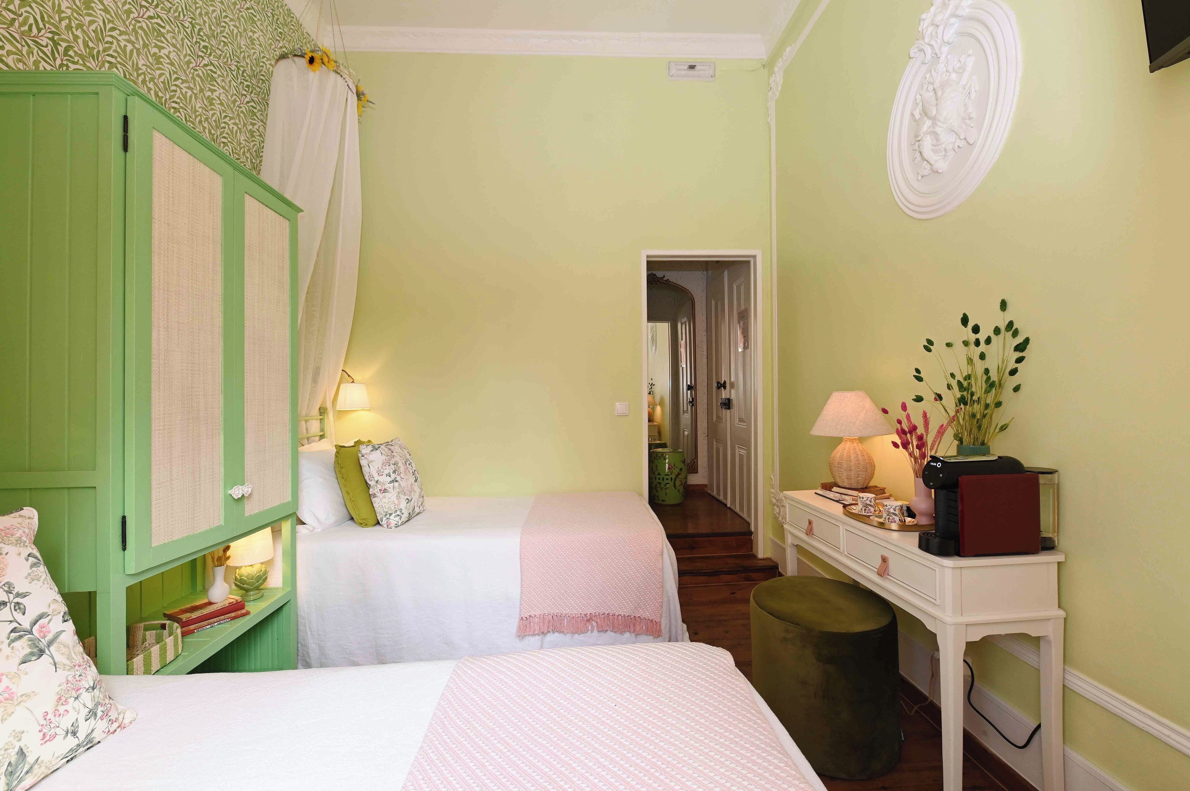 Een kamer met twee bedden, een groene garderobe, een witte console tafel met een lamp en een klein krukje.