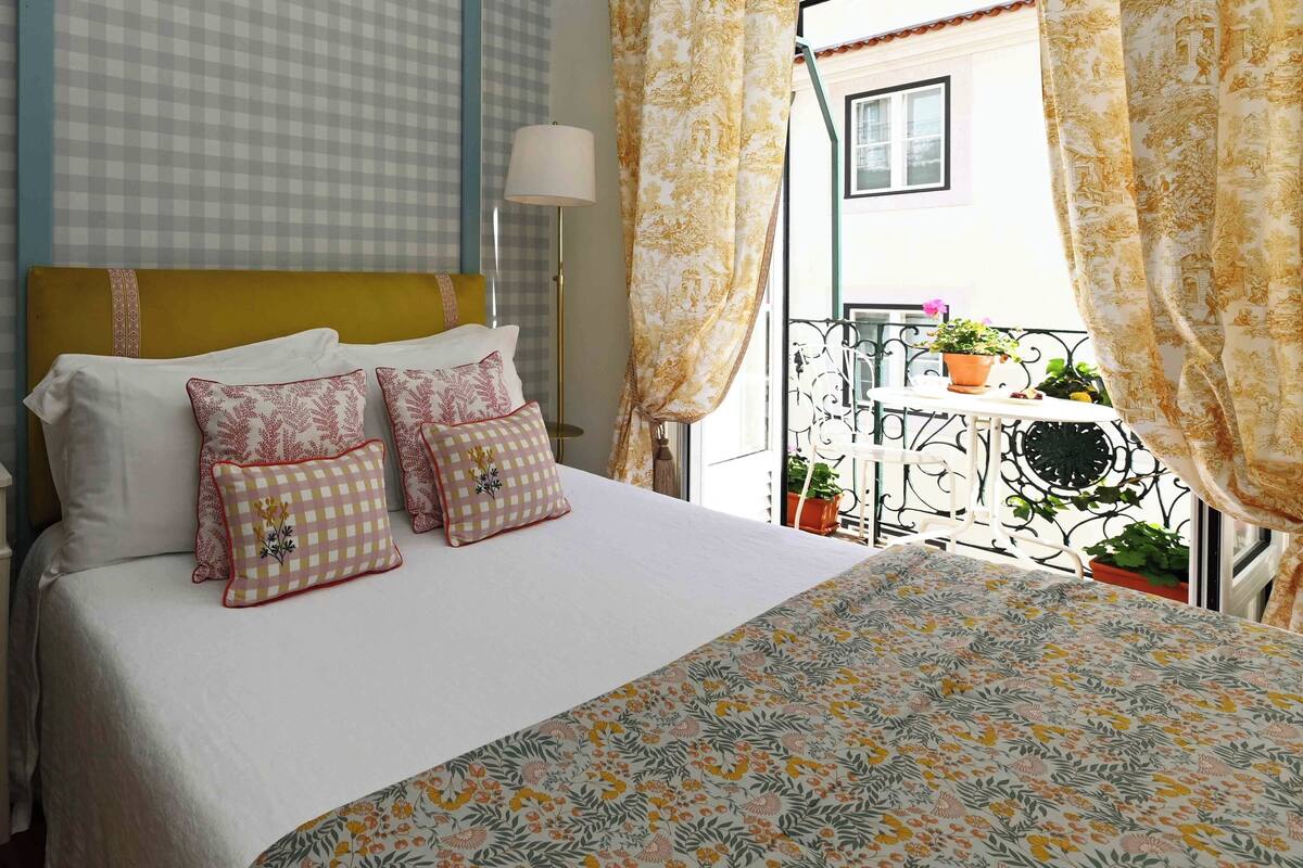 A hotel room with a bed, pillows, a lamp, and a balcony with potted plants.