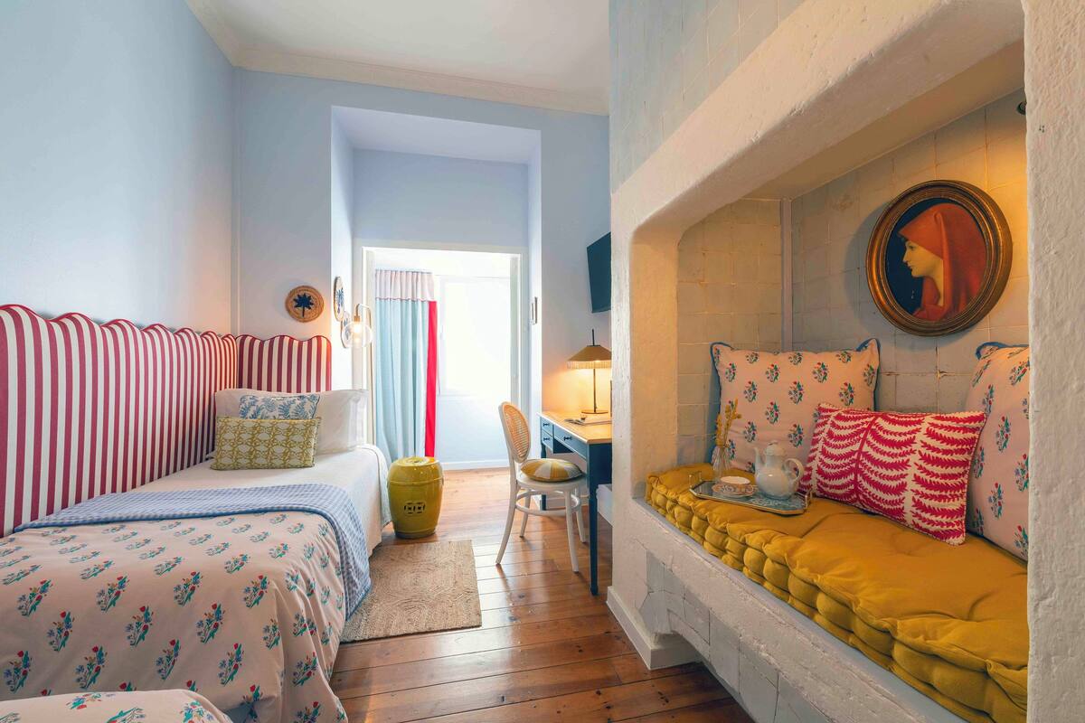 A cozy room with two beds, a desk, and a fireplace.