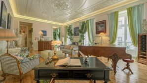 A room with a wooden floor, a black desk with a book, a green sofa, and a wooden cabinet. - Casinha das Flores (Lisbon)