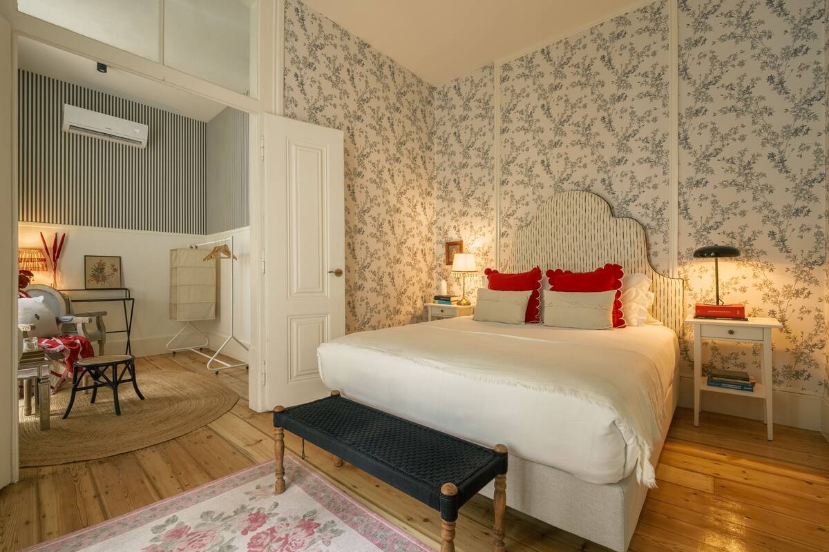 A bedroom with a large bed, a bench, a desk, and a chair.