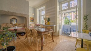 A dining area with a wooden table and chairs, a fireplace, and a view of the outside. - Casinha das Flores (Lisbon)