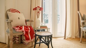 A cozy room with a wicker chair, a small round table, and a vase with flowers. - Casinha das Flores (Lisbon)