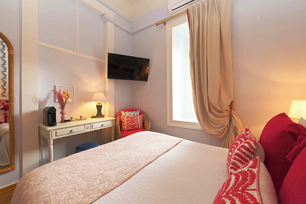 A hotel room with a bed, a desk, a television, and a window with curtains.