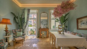 A room with a wooden floor, a dining table with chairs, a sofa, a chair, a lamp, and a large mirror. - Casinha das Flores (Lisbon)