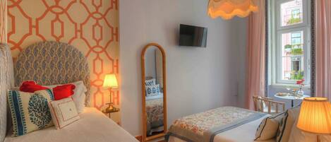A hotel room with two beds, a TV, a mirror, a window with curtains, and a table with a lamp.