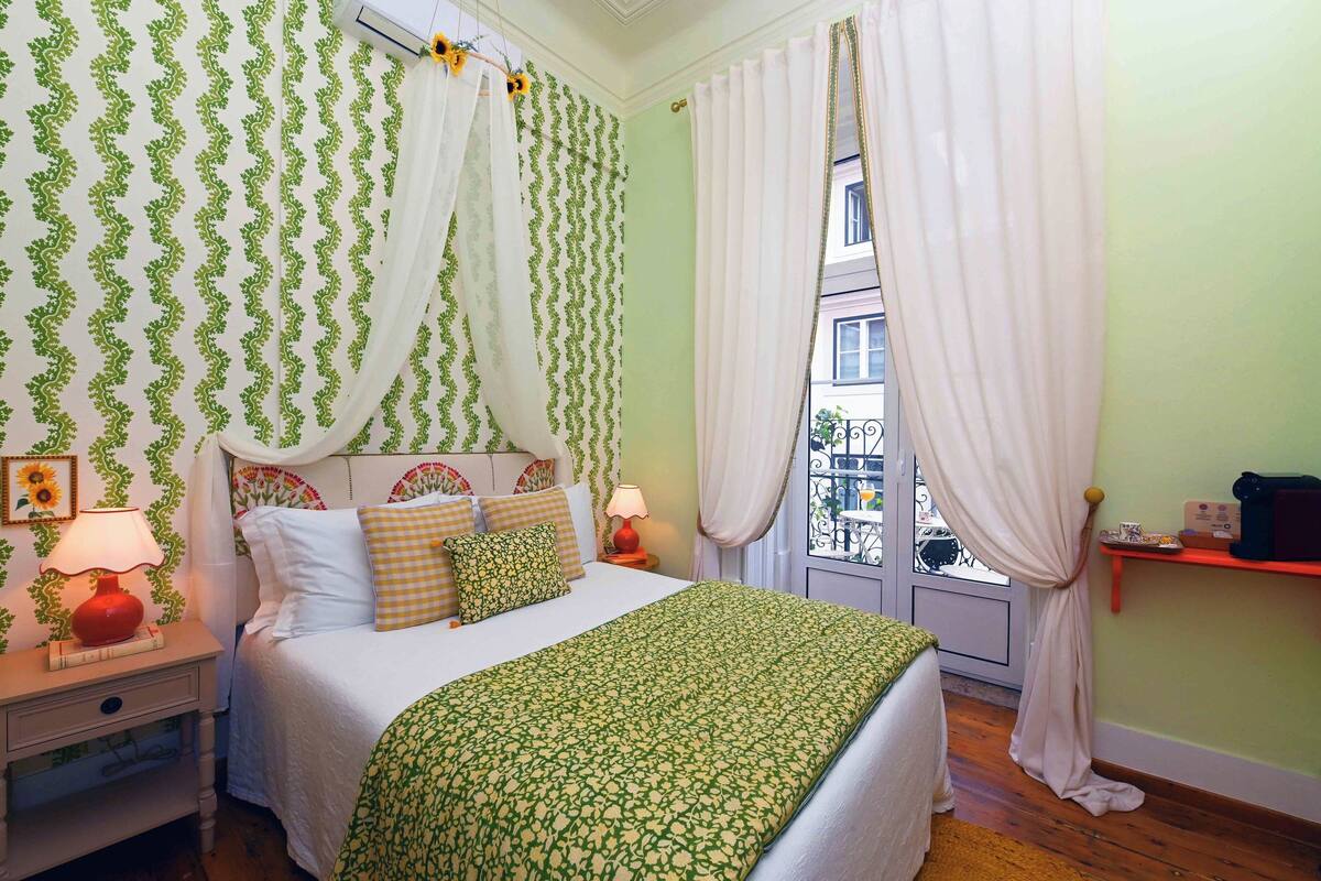 A bedroom with a bed, curtains, a nightstand, a lamp, and a window with a view.