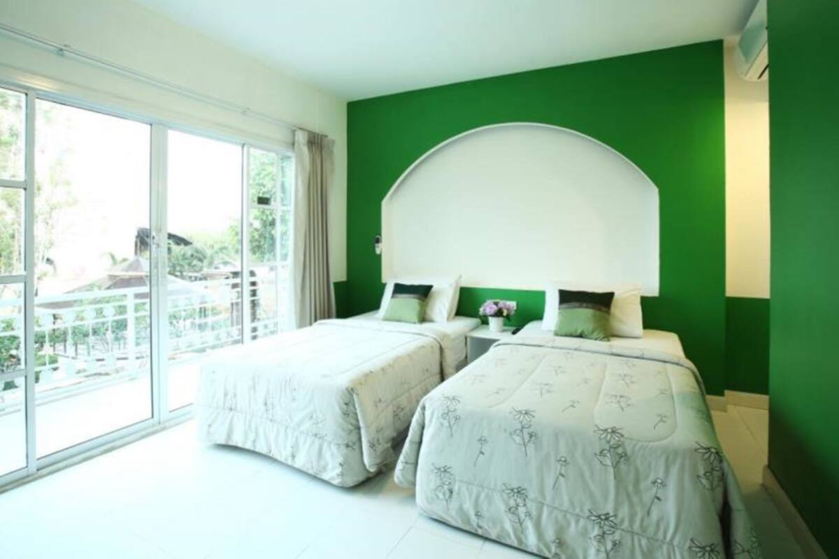 Une chambre d’hôtel avec deux lits, une grande fenêtre et un mur d’accent de couleur verte.