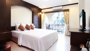 Habitación de hotel con una cama grande, televisión, escritorio con cafetera y balcón con mobiliario exterior.