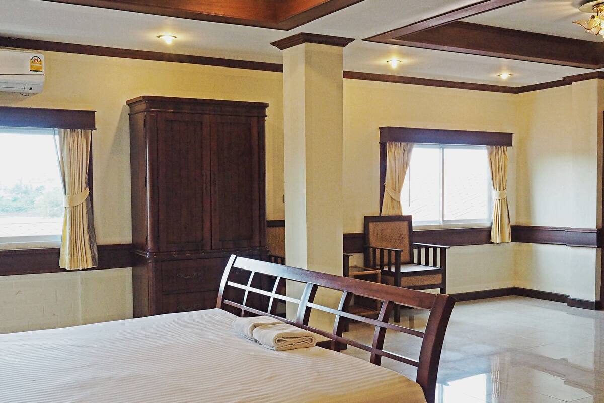 Une chambre d’hôtel avec un grand lit, une armoire en bois, une chaise et une fenêtre avec des rideaux.