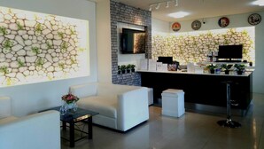 Zona de recepción con diseño moderno, que presenta una pared de piedra con plantas, un televisor de pantalla plana, un mostrador de recepción y un área de estar.