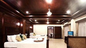 Habitación de hotel con dos camas, televisión y una zona de comedor al fondo.