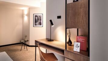 Una habitación de hotel moderna con cama, escritorio, silla, estantería y lámpara.