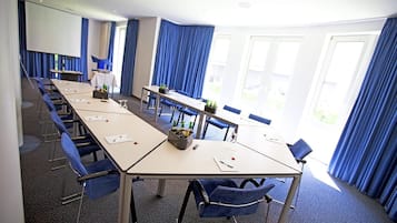 Ein Konferenzraum mit einem langen Tisch, blauen Stühlen und einer Projektorleinwand.