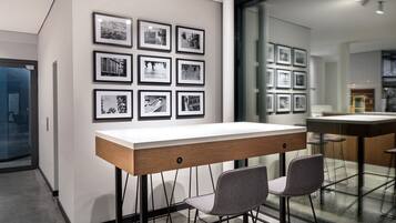 Un comedor moderno con una mesa larga y dos taburetes de bar, una pared con fotografías enmarcadas y un panel de vidrio que separa el comedor de otro espacio.