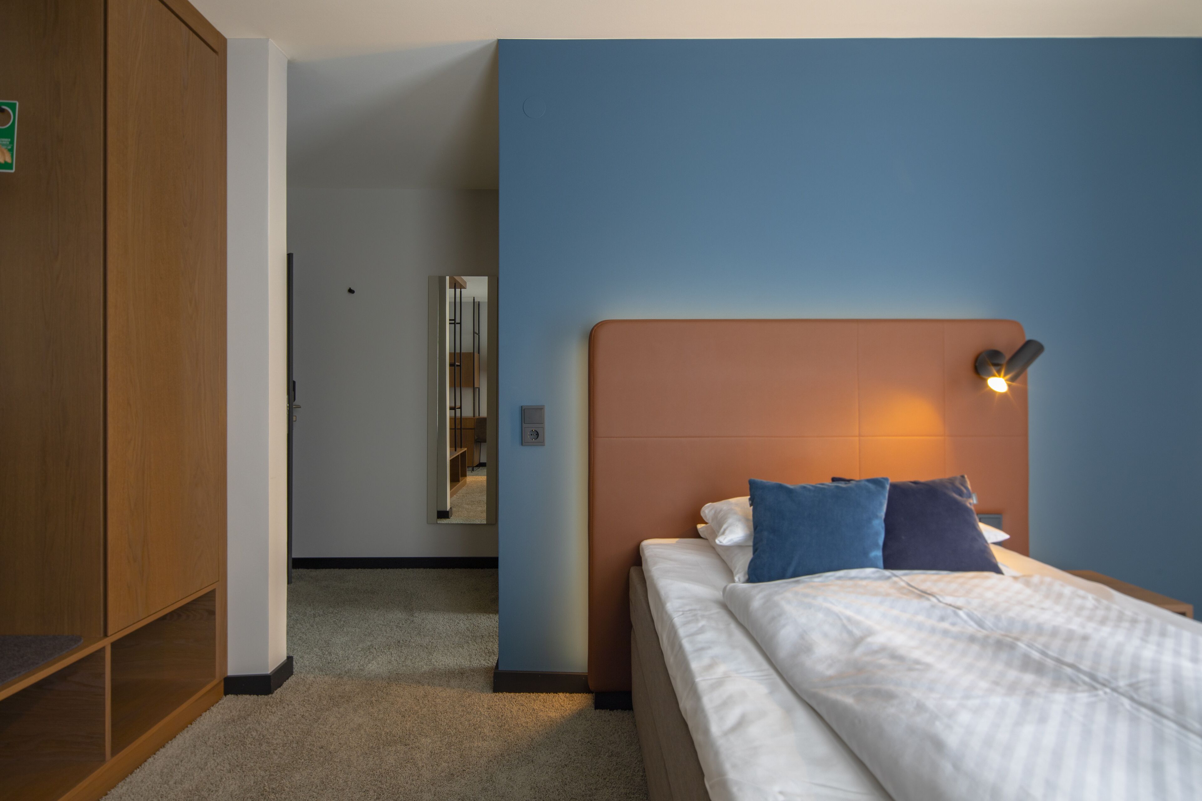 Une chambre d’hôtel comprenant un lit, une table de chevet, une lampe fixée au mur et une armoire en bois.