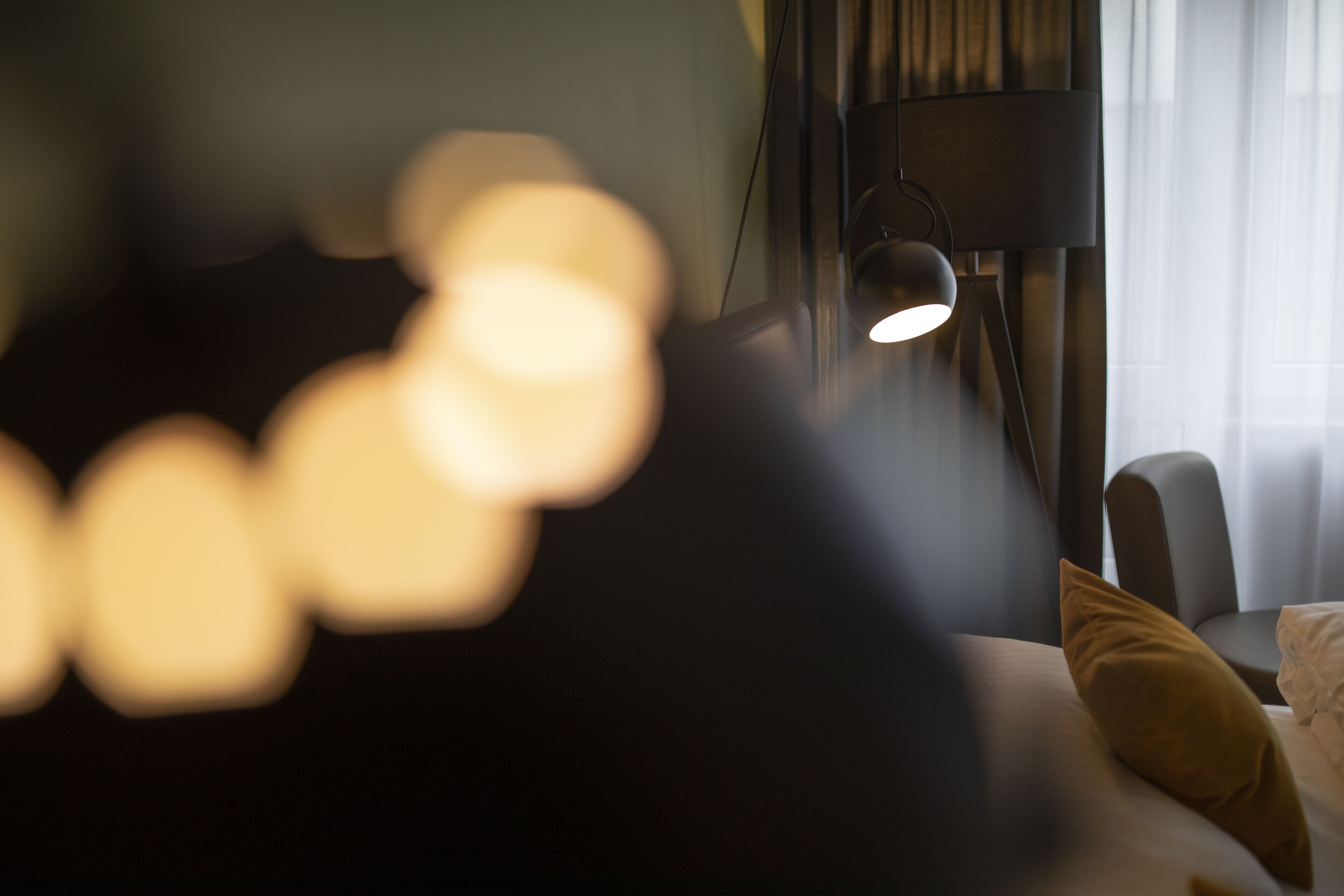 A blurred view of a bed with a pillow, a lamp, and a window with curtains.