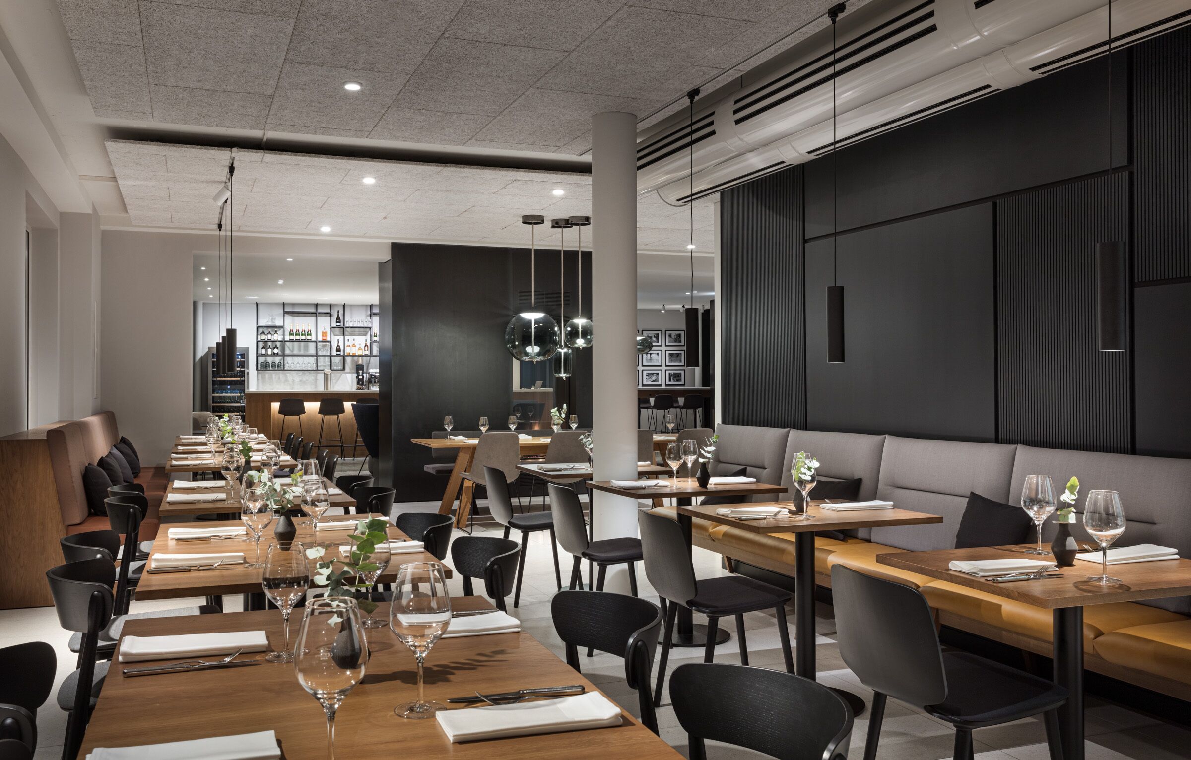 Ein modernes Restaurant mit langen Holztischen, schwarzen Stühlen und hängenden, kugelförmigen Leuchten.