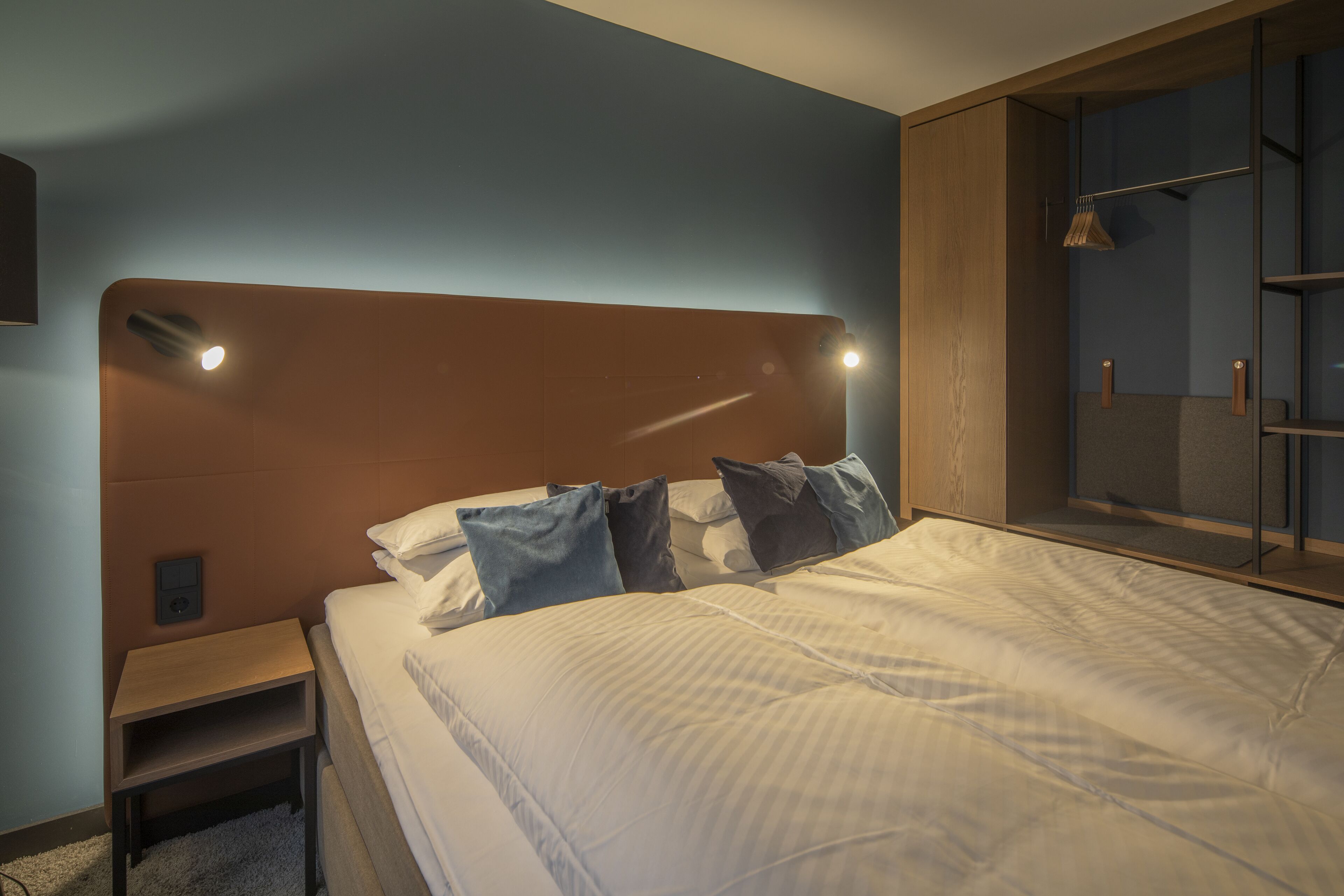 A neatly made bed with a wooden headboard, a bedside table, and a wardrobe with a mirror.