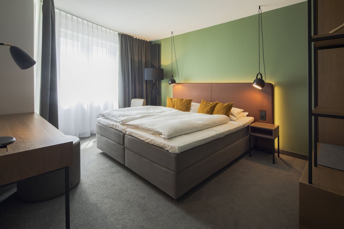 Quarto de hotel com uma cama grande, uma escrivaninha, uma cadeira e uma mesa de cabeceira.