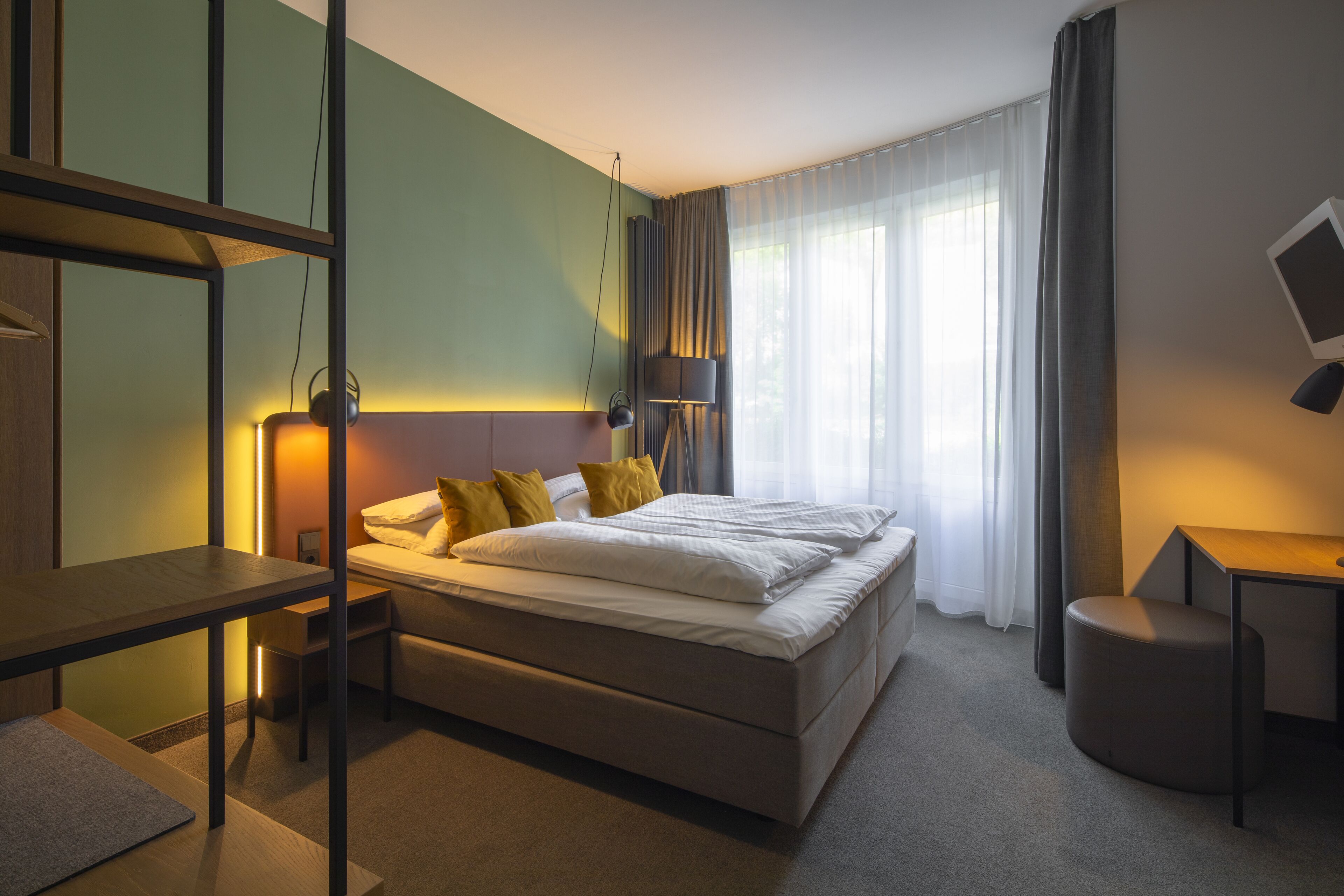 A modern hotel room with a large bed, bedside tables, a desk, and a view of the outdoors.