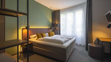 A modern hotel room with a large bed, bedside tables, a desk, and a view of the outdoors.