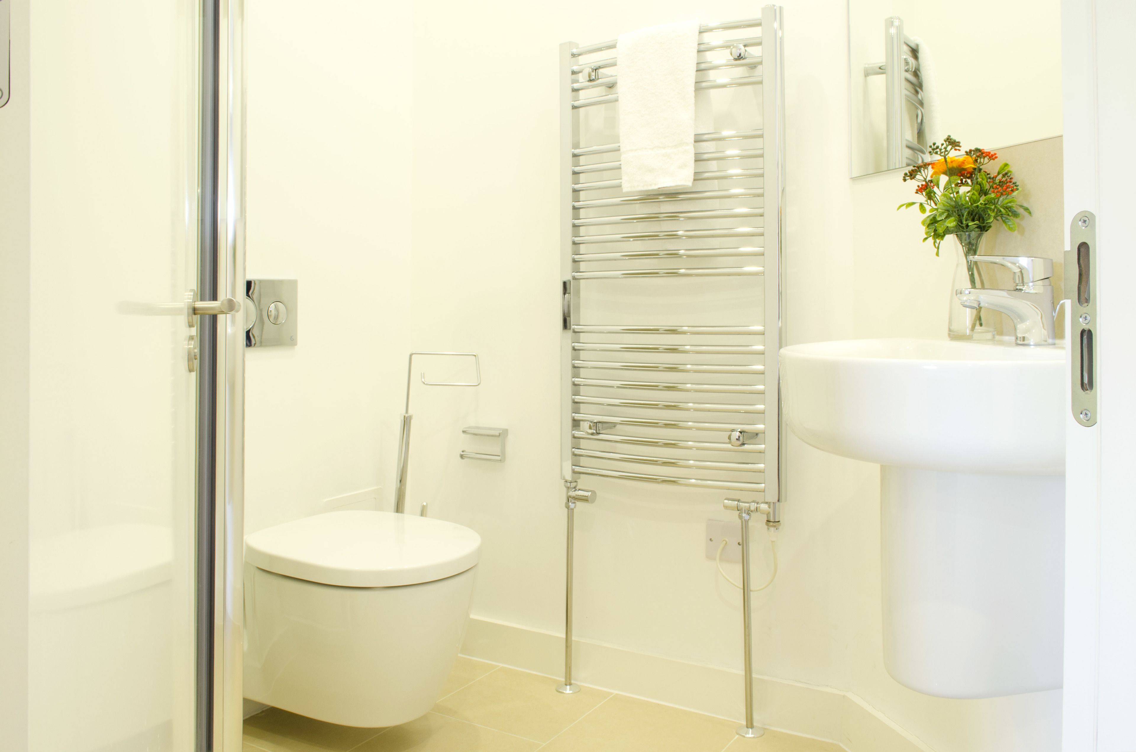 A modern bathroom with a toilet, a glass shower enclosure, a towel rack, and a sink with a mirror above it.