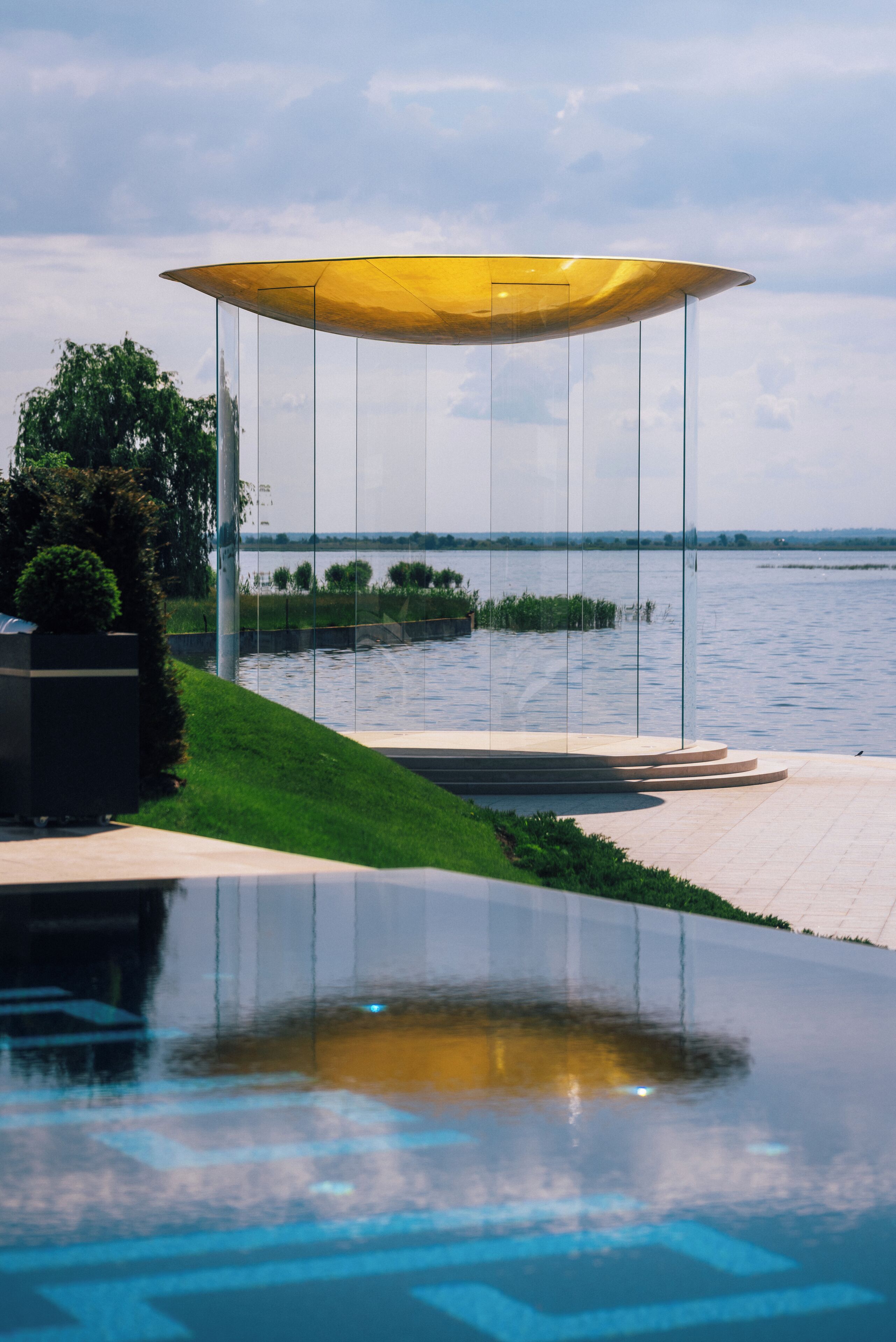 Un área de piscina exterior moderna con cerramiento de vidrio y una sombrilla amarilla.