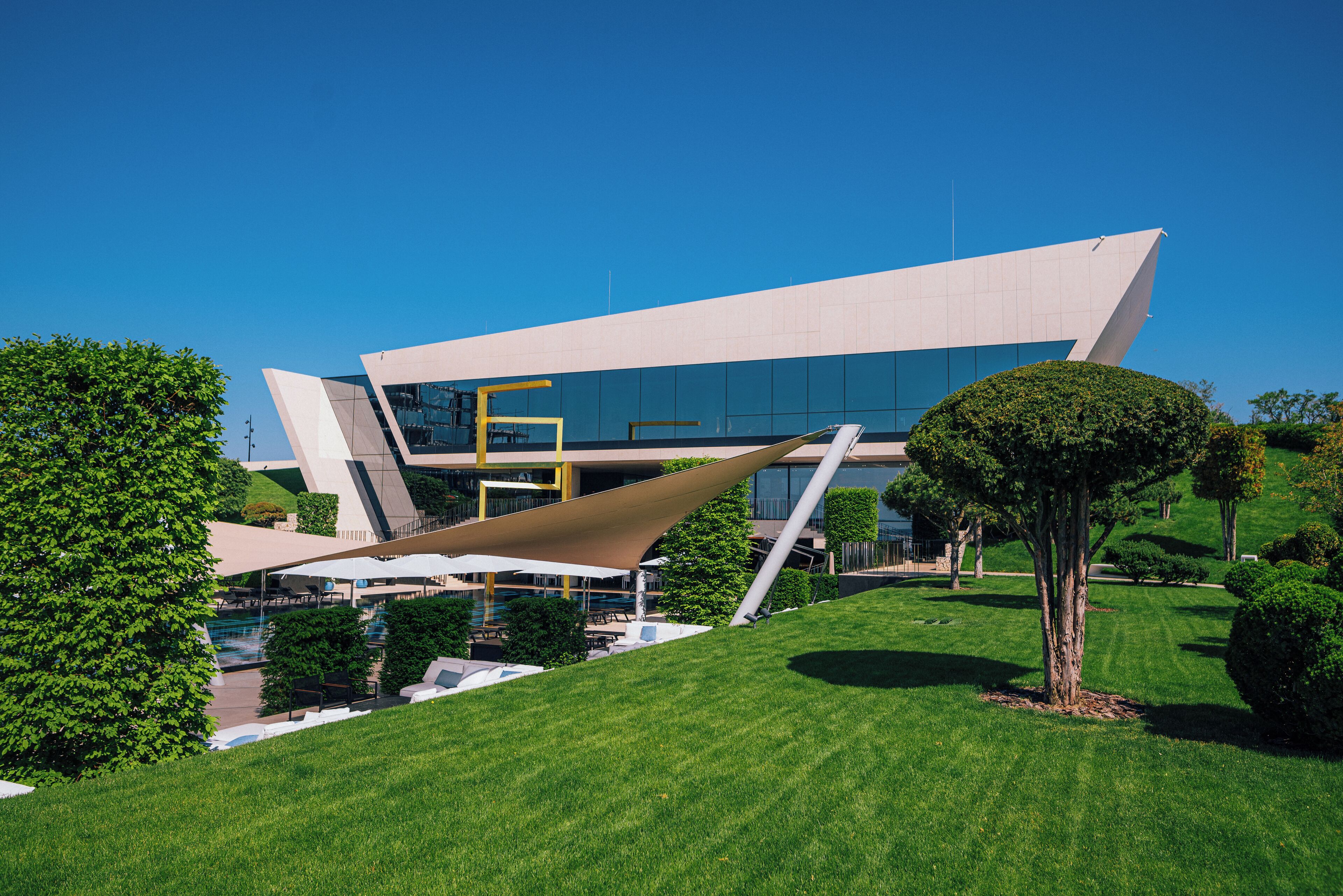 Un edificio moderno con un diseño angular único, rodeado de céspedes verdes y árboles bien cuidados.