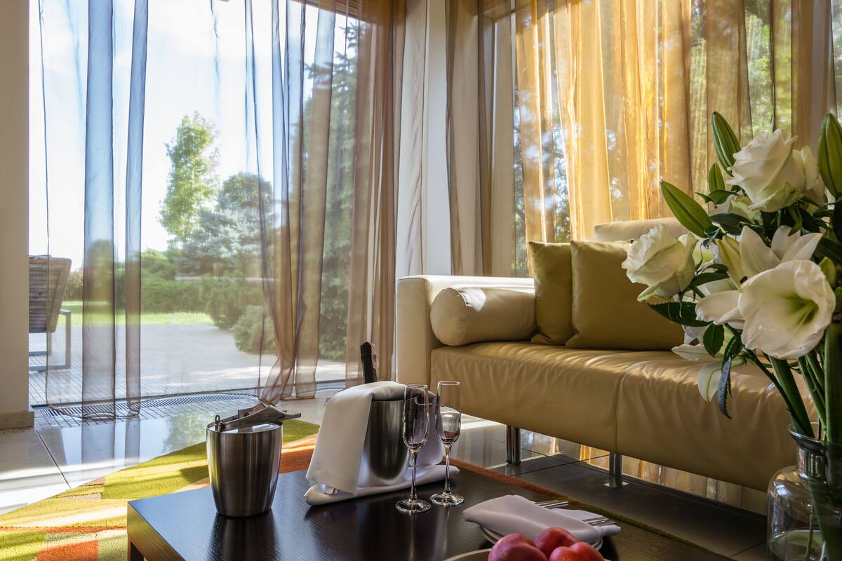 Habitación con sofá, una mesa de comedor con un florero y vista a espacios verdes.