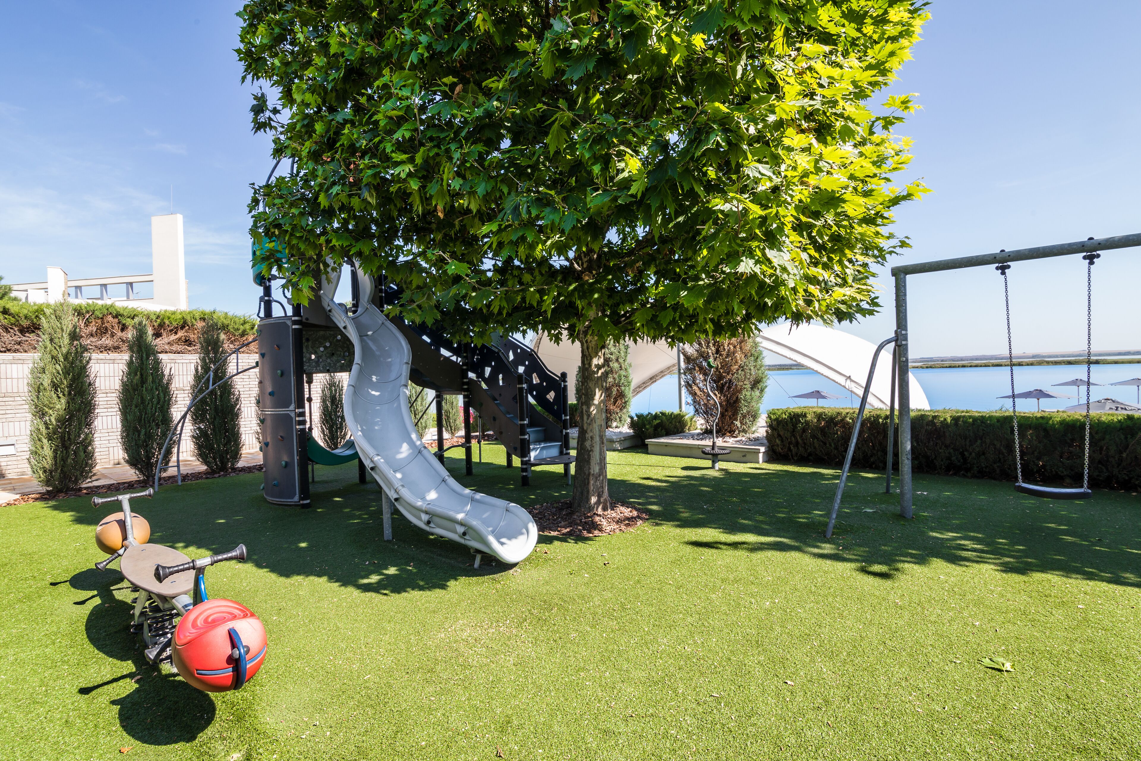 A playground with a slide and swings, surrounded by well-maintained grass and trees.