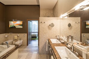Un baño moderno con varios lavamanos, un bidé y una ducha. Hay un espejo grande y un cuadro en la pared.