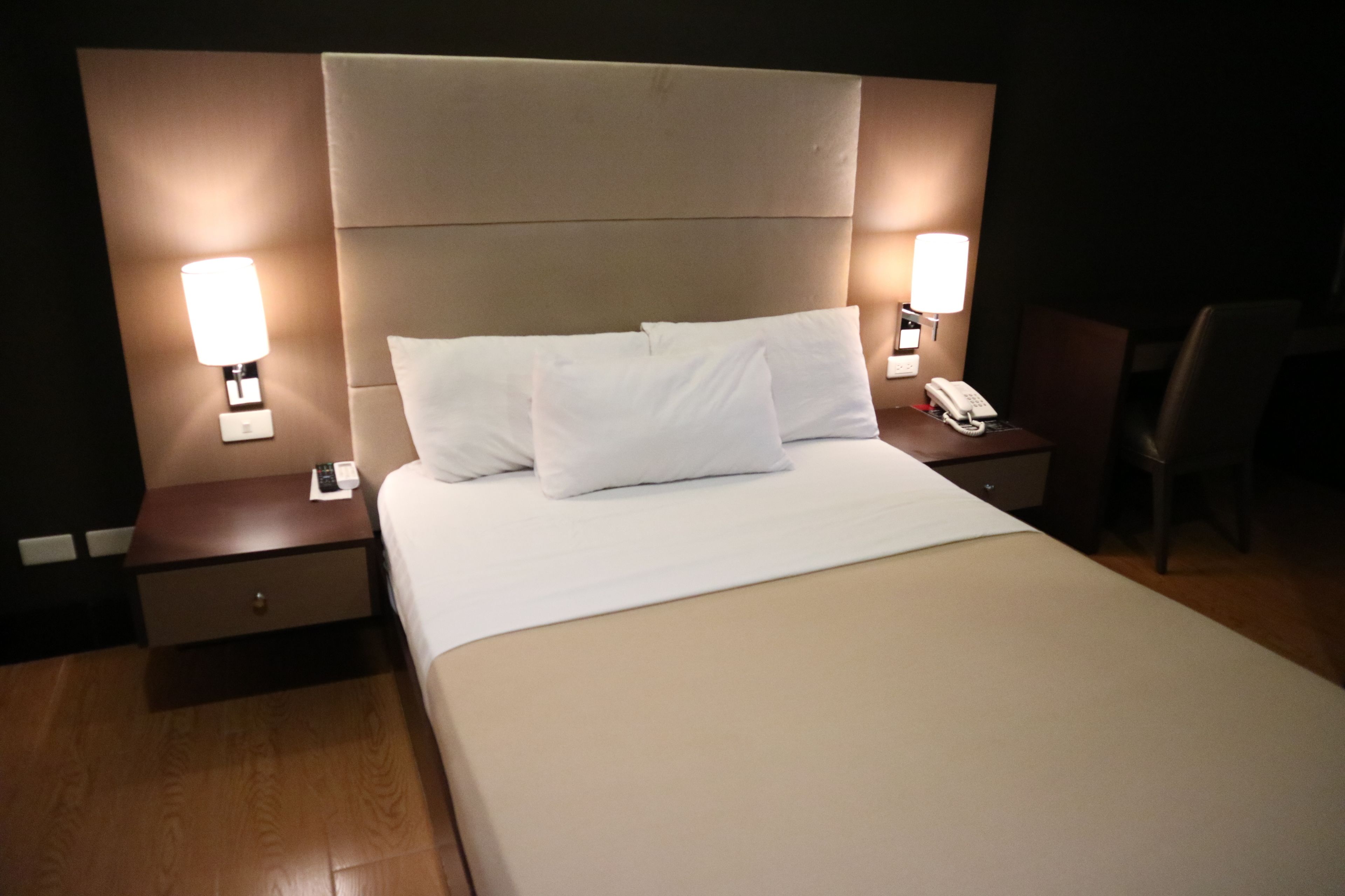 A hotel room with a large bed, two bedside tables with lamps, a nightstand, and a chair.