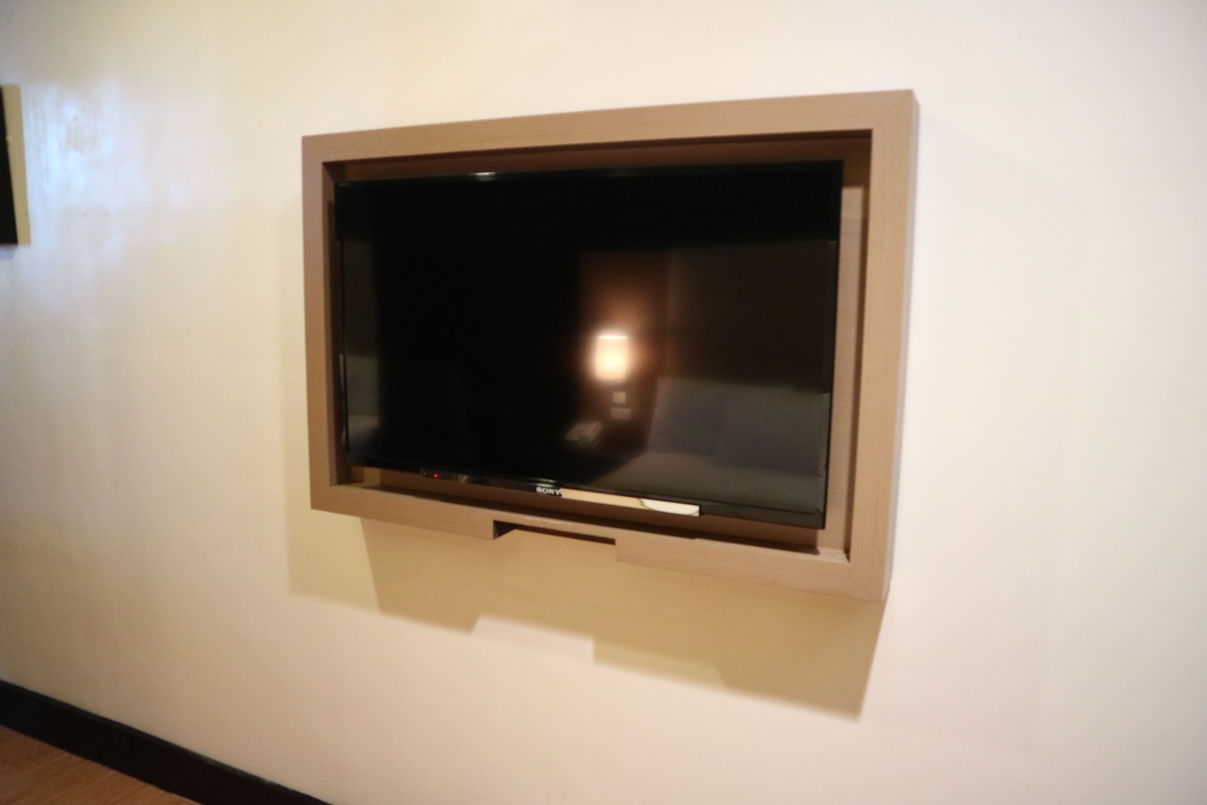 A wall-mounted television in a room with a plain white wall and a wooden floor.