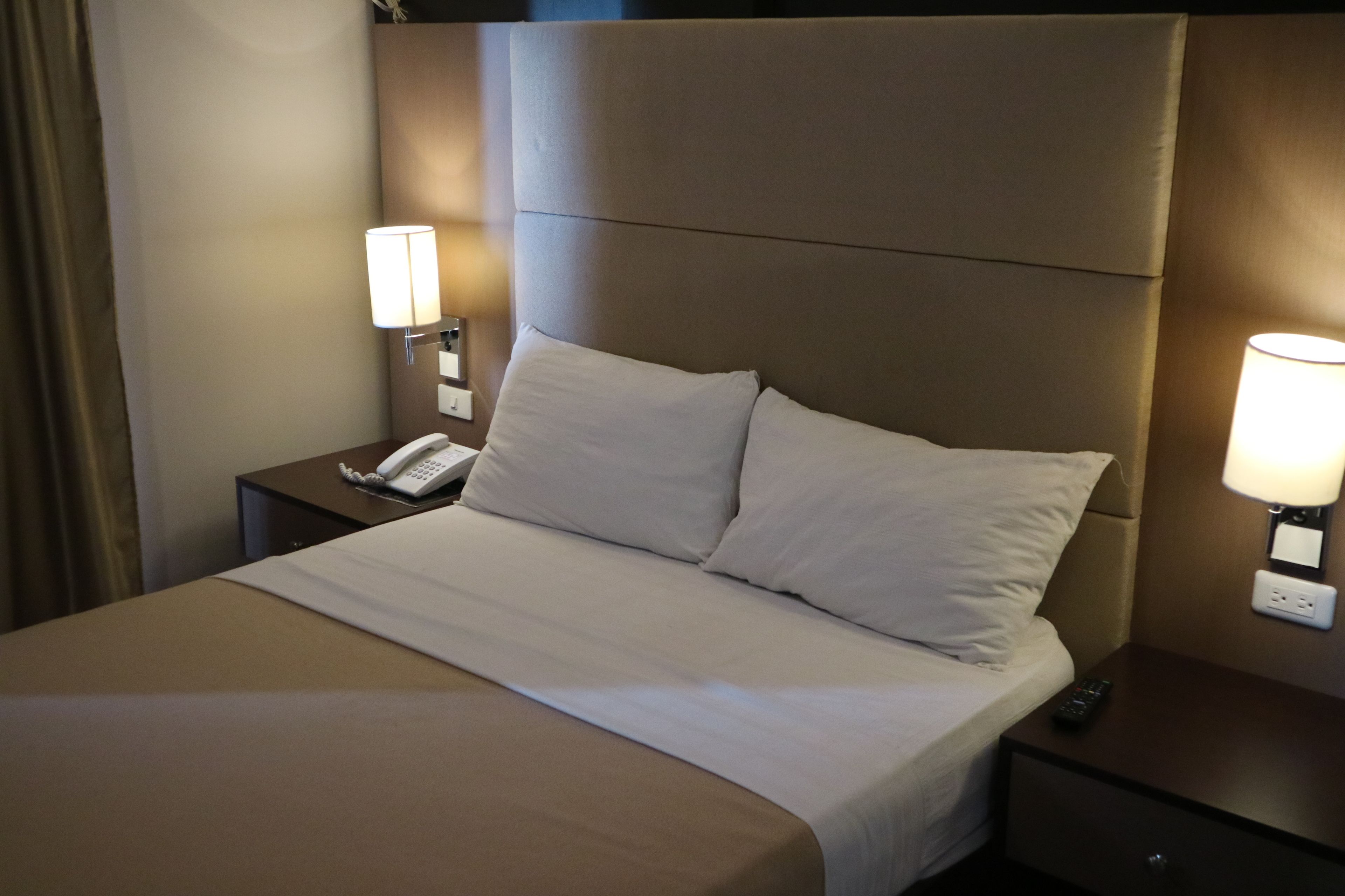 Ein Hotelzimmer mit einem großen Bett, zwei Nachttischen, einem Telefon und Wandlampen.