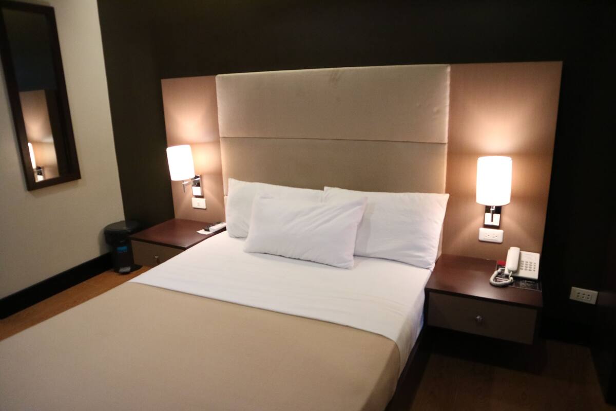 A hotel room with a large bed, two bedside tables, and wall-mounted lamps.