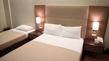 A hotel room with two beds, a nightstand with a phone, and wall-mounted lamps.