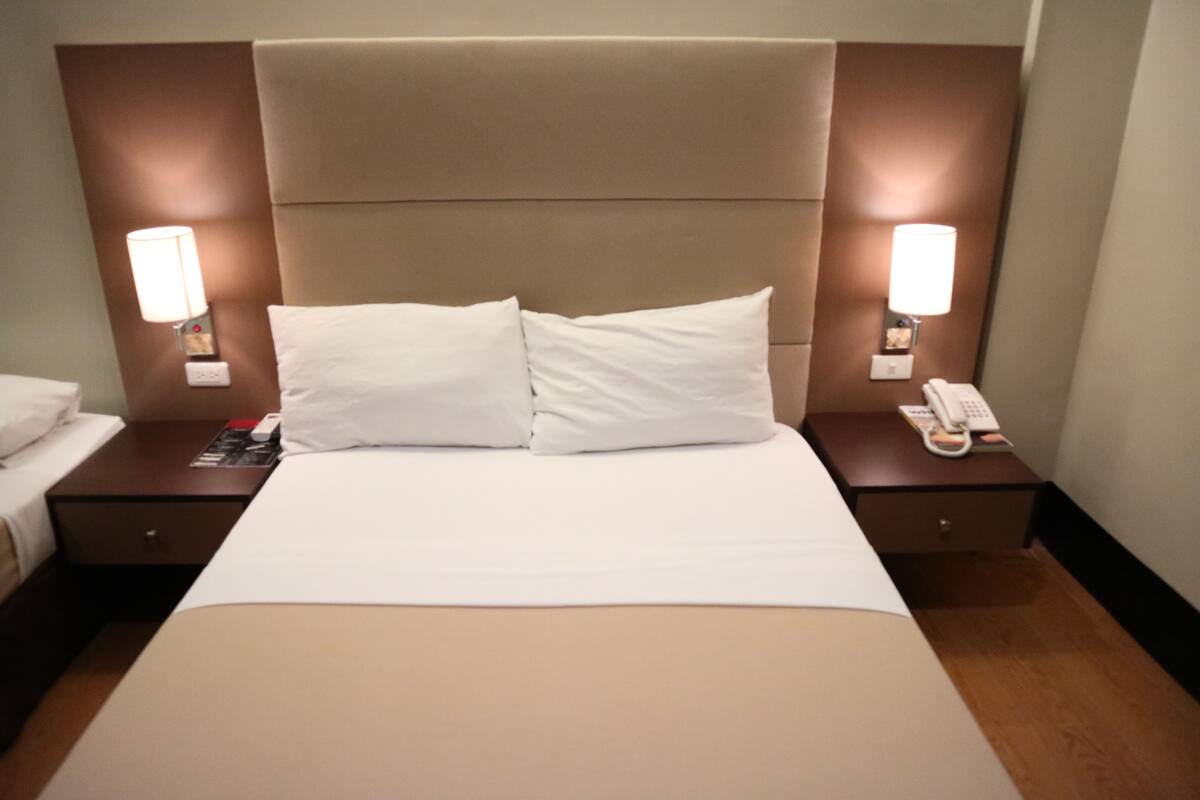 A hotel room with a large bed, two bedside tables, a nightstand, and a wall-mounted telephone.