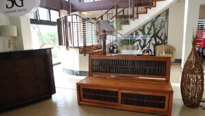 Un vestíbulo con una escalera, bancos de madera, un mostrador de recepción y un gran jarrón decorativo.