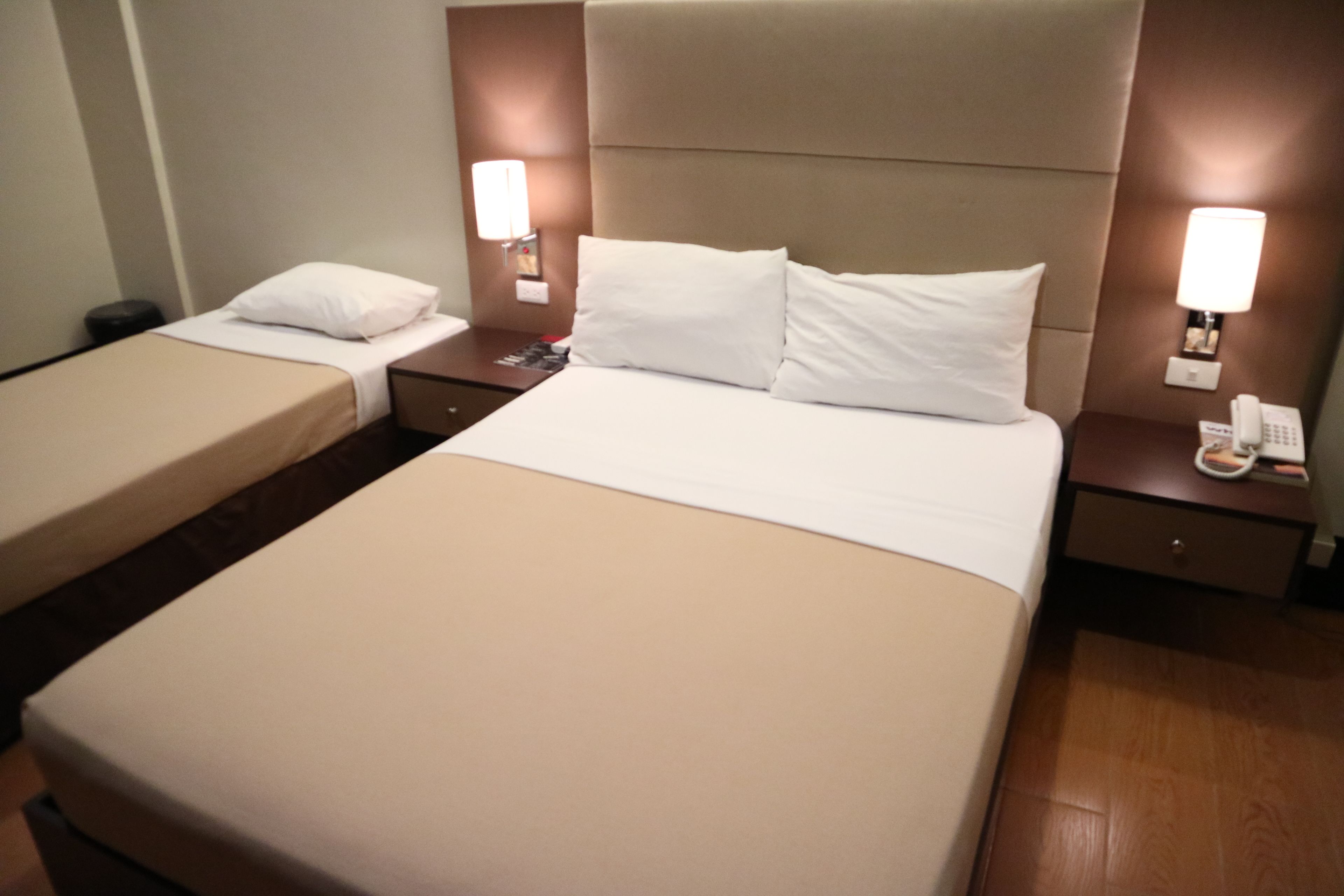 A hotel room with two single beds, a large bed, and a nightstand with a phone.